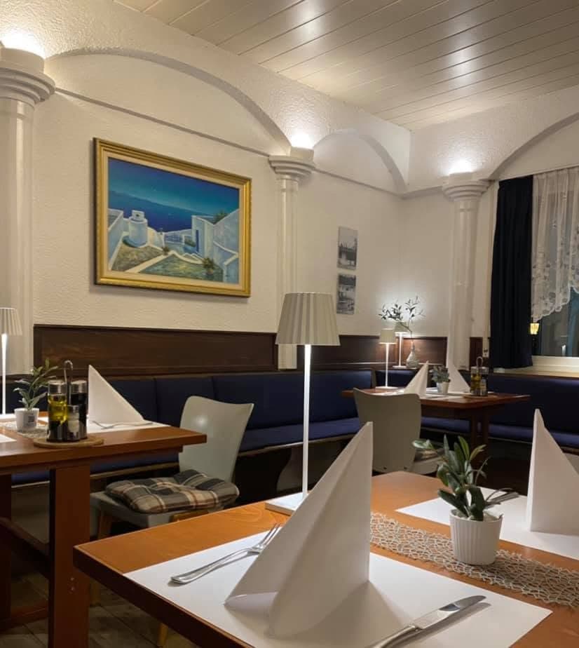 Eingedeckte Tische am Abend im Restaurant Zeus mit Santorini-Gemälde an der Wand